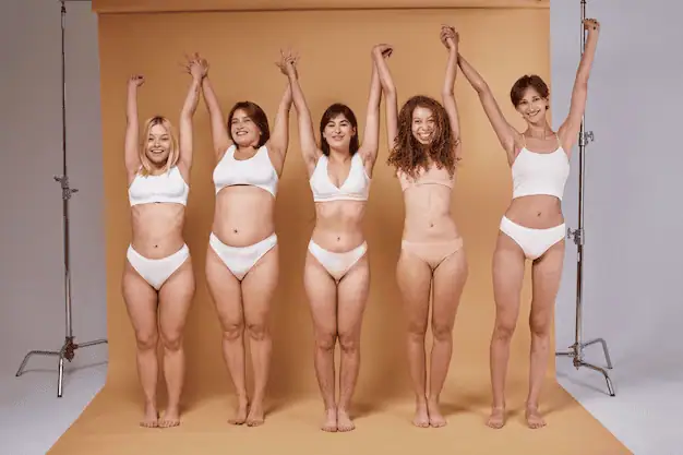 Empowered diverse women celebrating body positivity in underwear, smiling with arms raised in a studio setting. A powerful image promoting confidence, self-love, and inclusivity for all body types.