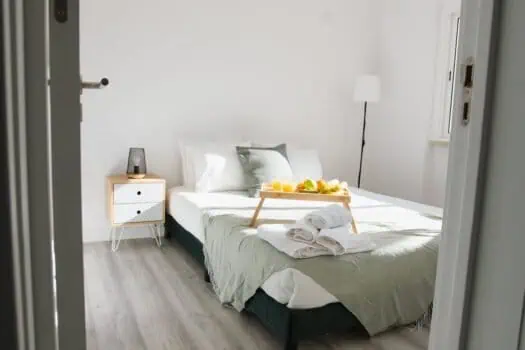 Bright minimalist bedroom with white walls, neatly made bed with fresh towels, natural light, and modern decor, ideal for a comfortable stay.