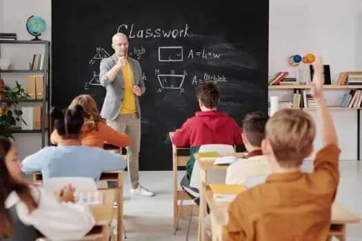 Engaging classroom scene with teacher explaining maths to students at blackboard in school setting.