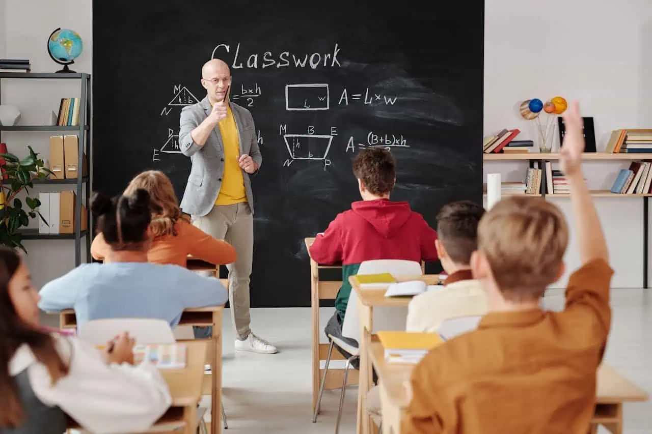 Engaging classroom scene with teacher explaining maths to students at blackboard in school setting.