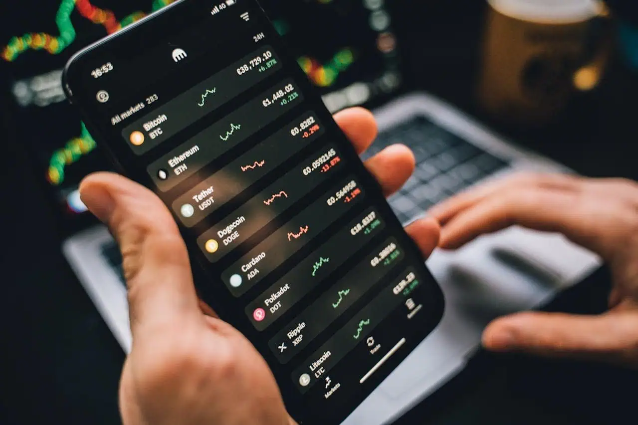 Cryptocurrency trading app displaying live Bitcoin, Ethereum, and Dogecoin market data on smartphone screen. Person monitoring digital assets and crypto investment performance.