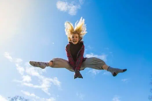 Girl jumping high in the sky on a sunny day, expressing joy and freedom, outdoor activity, vibrant blue sky, casual clothing, and autumnal season, perfect for happiness, adventure, and outdoor lifestyle themes.