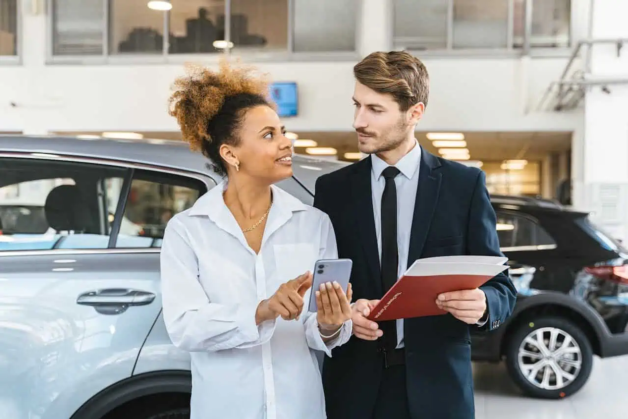 Meeting between a sales advisor and a customer at a car dealership, discussing vehicle options and financing, in a modern showroom environment.