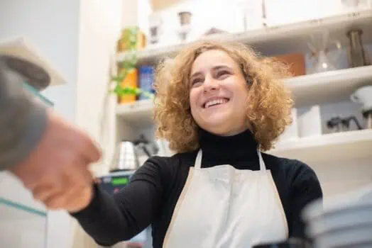 Young woman smiling in kitchen while wearing apron, engaging with elderly person, promoting social inclusion and community support for people with disabilities, inclusive environment, Prowess organization.