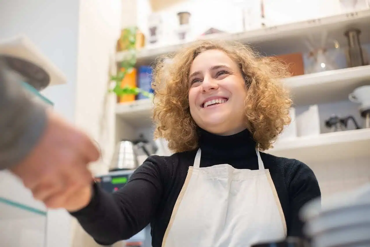 Young woman smiling in kitchen while wearing apron, engaging with elderly person, promoting social inclusion and community support for people with disabilities, inclusive environment, Prowess organization.