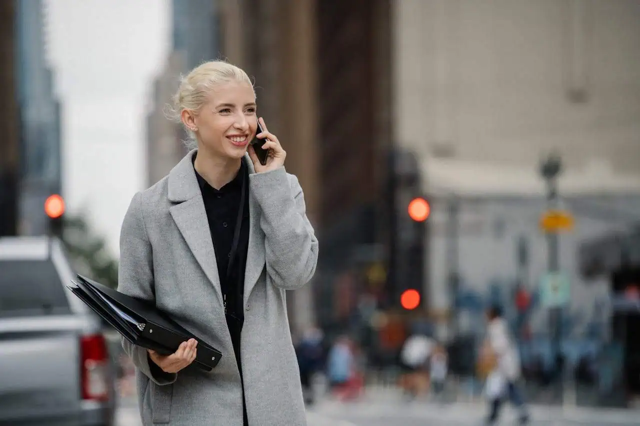 Professional woman in business attire talking on mobile phone while walking in city centre, holding a folder, urban background, city life, corporate communication, modern professional.