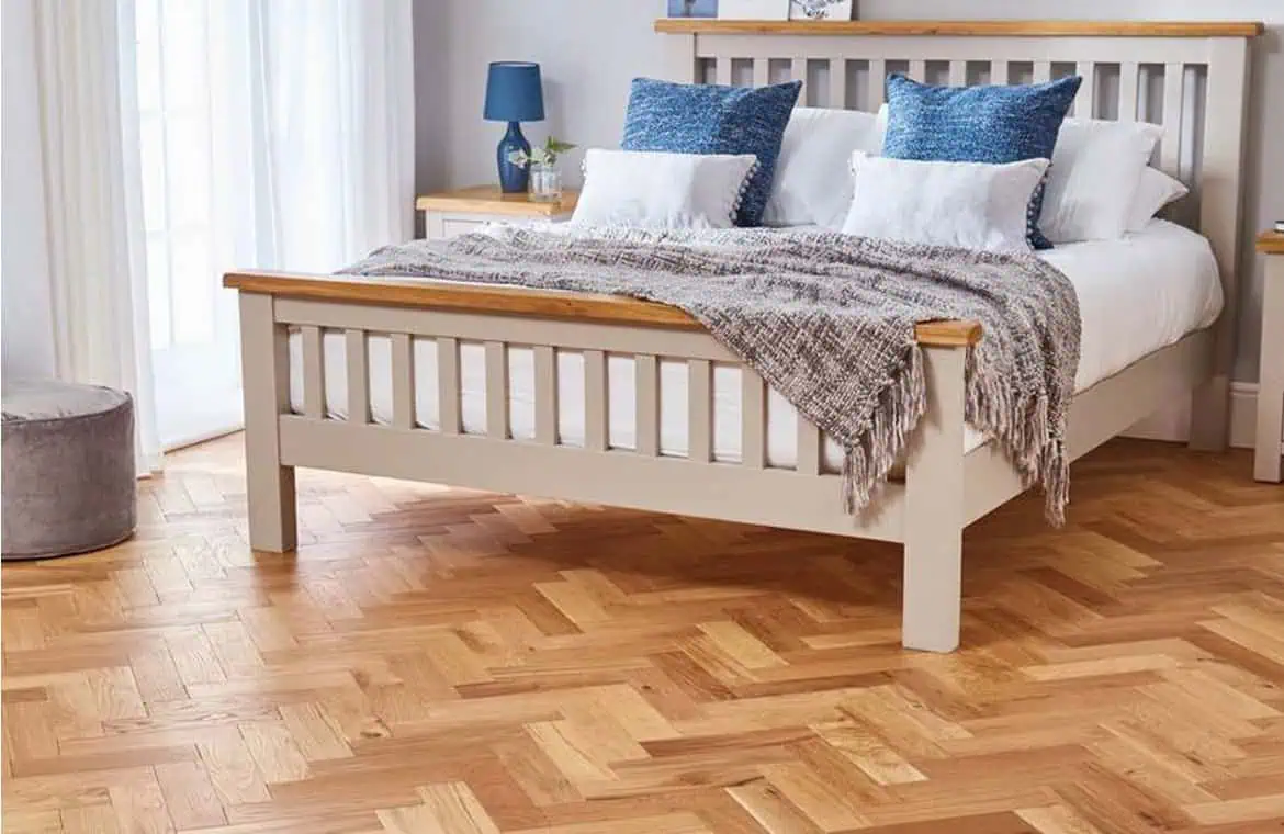 L-shaped hardwood flooring in a modern bedroom with a white bed and blue cushions, bright natural light, cosy decor.