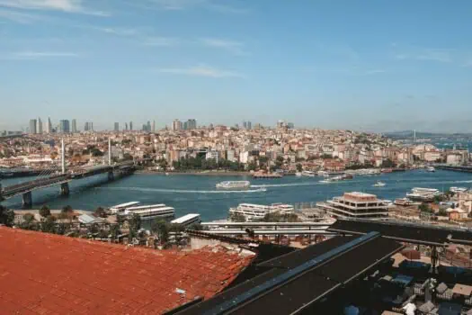Vibrant cityscape of Istanbul showcasing the Bosphorus Strait, modern skyscrapers, historic architecture, and boat-filled waters under a clear blue sky.