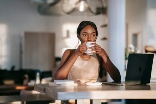 Fresh young woman enjoying coffee at work desk with laptop in modern cafe setting, representing empowerment, productivity, and focus for women in the workplace.