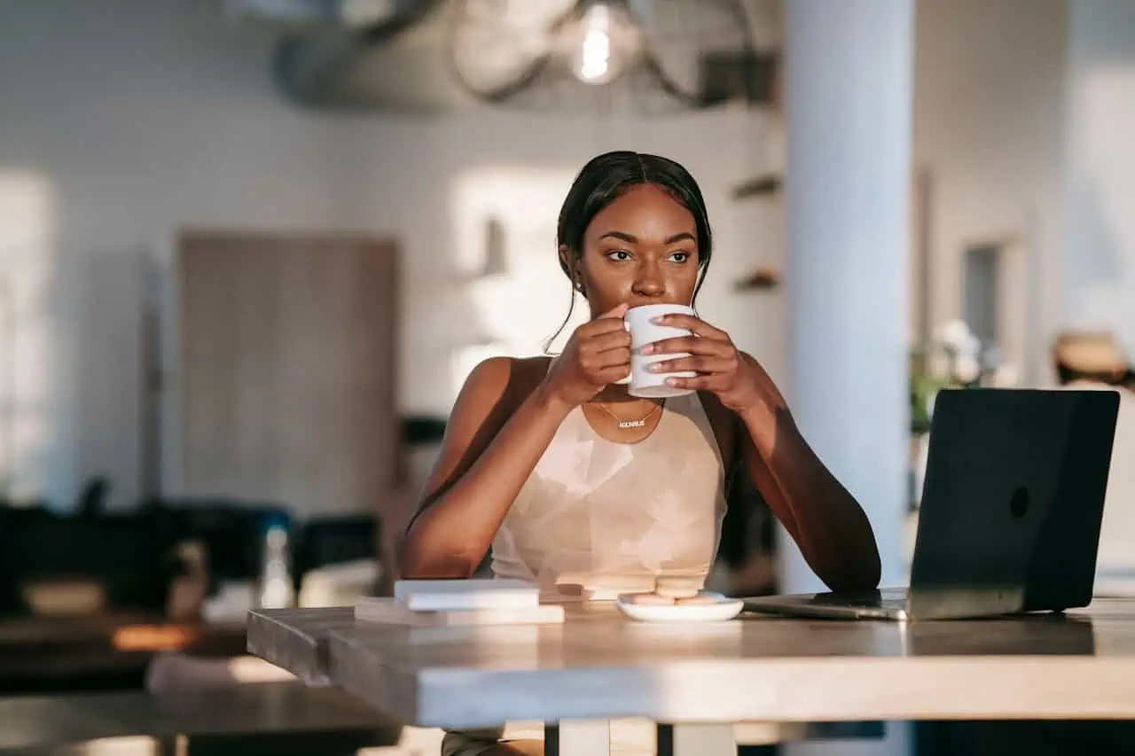Fresh young woman enjoying coffee at work desk with laptop in modern cafe setting, representing empowerment, productivity, and focus for women in the workplace.