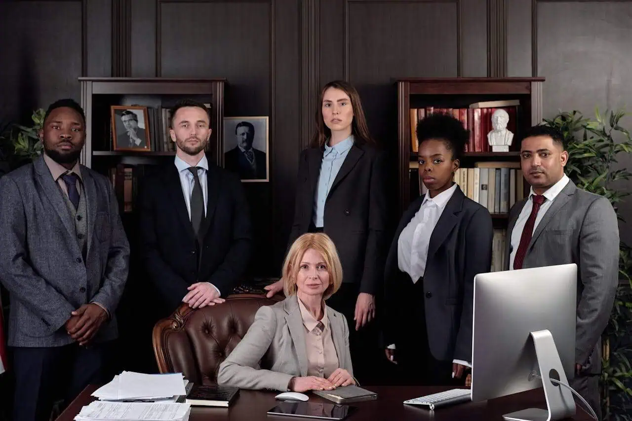 Diverse group of professionals in formal business attire posing in an office setting, highlighting teamwork, diversity, and leadership. Suitable for corporate, legal, or organisational themes.