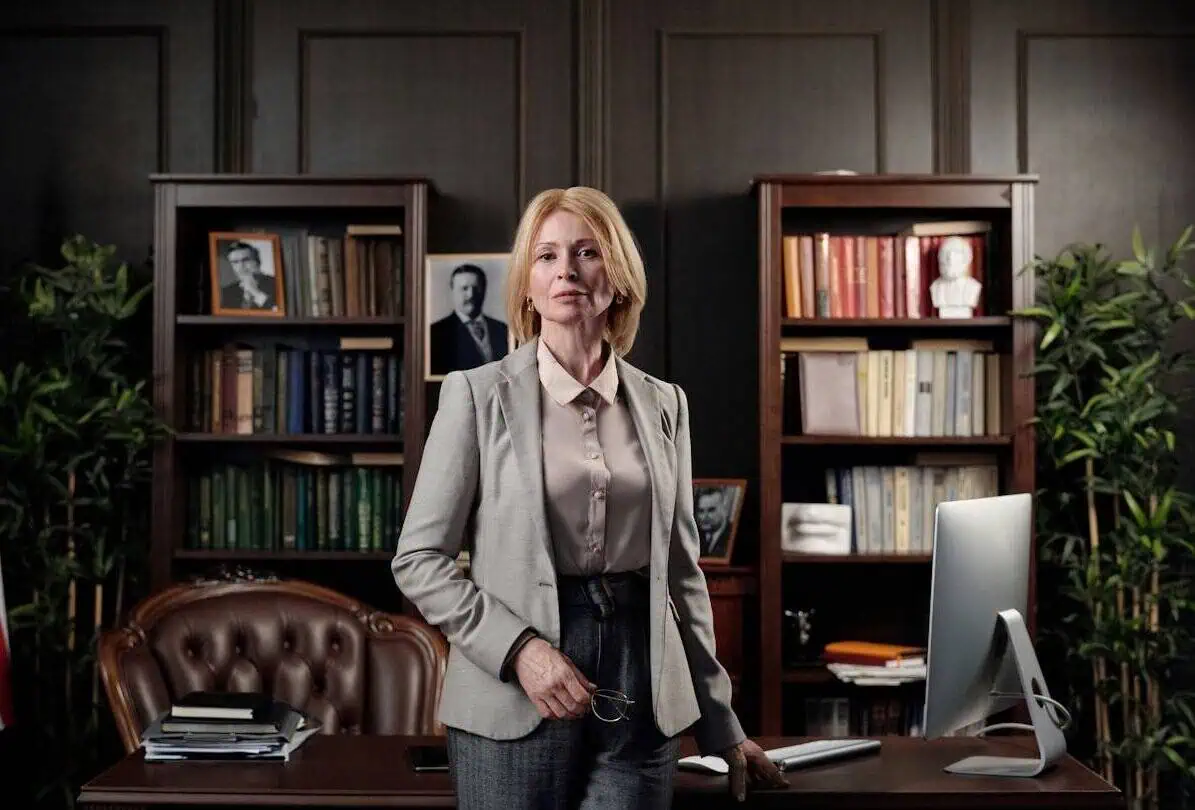 Professional woman in office with bookshelves and desktop computer, businesswoman in formal attire, work environment, executive office, corporate setting, Prowess organization image.