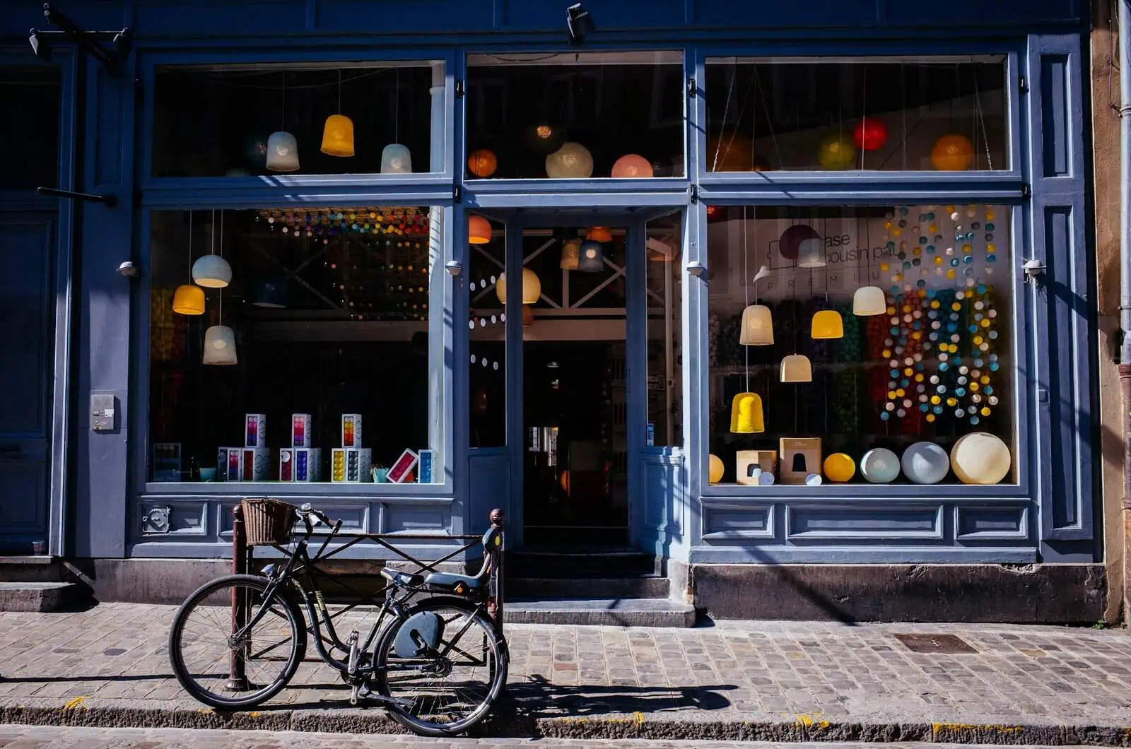 Colourful lighting shop display with hanging pendant lamps and decorative spheres in a blue storefront, promoting modern lighting solutions and home décor accessories in a stylish urban setting.
