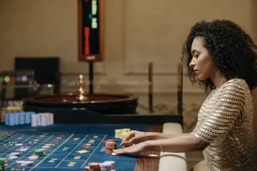 Woman playing roulette, casino gaming, gambler, casino table with chips, luxury casino environment, high-stakes gambling, elegant attire, betting, gaming entertainment, woman engaged in casino game.
