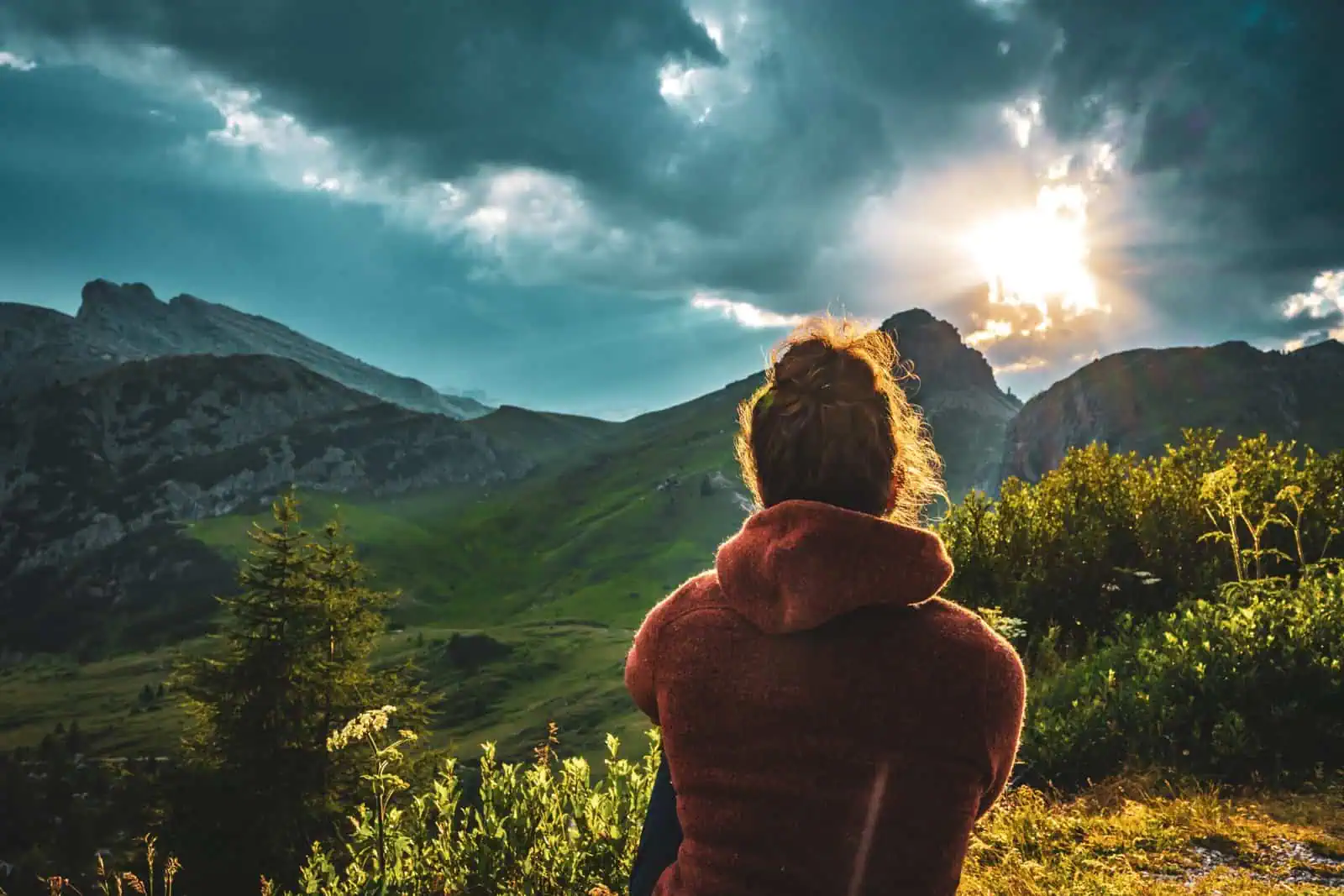 A woman enjoying the scenic mountain landscape during sunset, surrounded by lush greenery and dramatic clouds, capturing moments of outdoor exploration and nature's beauty.