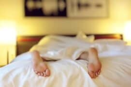 Bedroom with person lying in bed, feet visible, cozy and warm atmosphere, night-time setting, relaxing sleep environment, soft lighting, comfortable bedding, hotel or home bedroom, restful sleep scene.