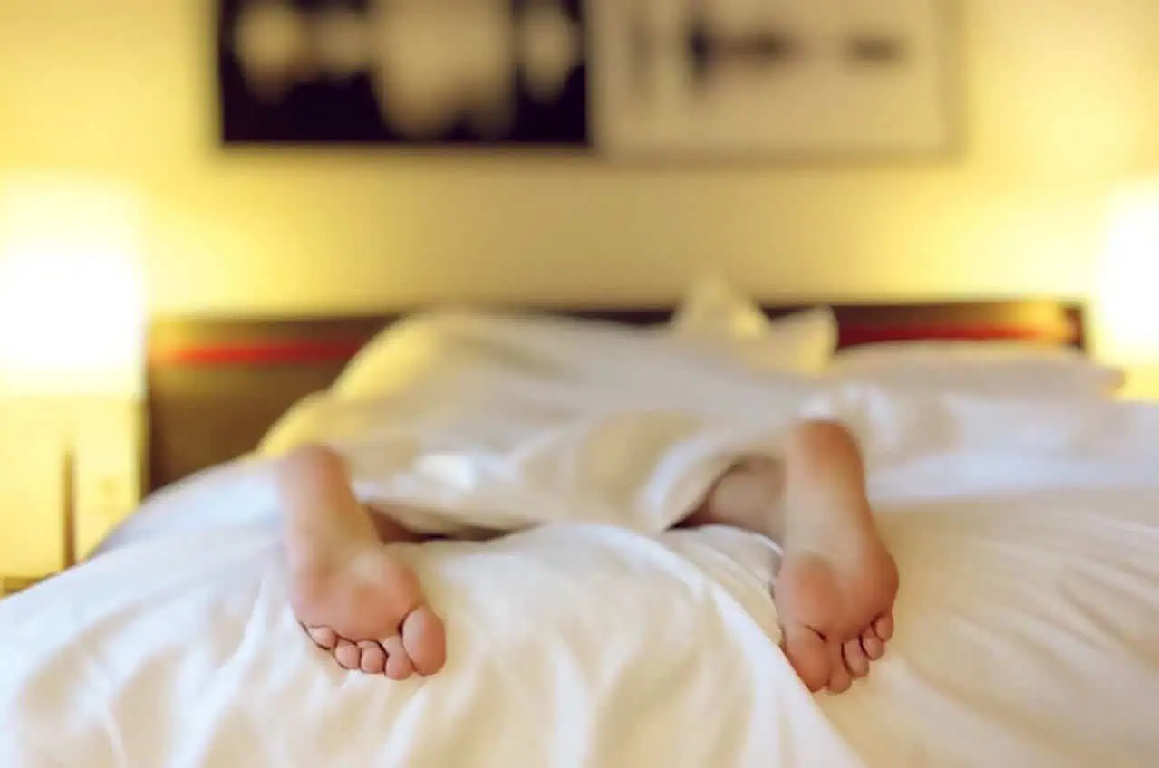 Bedroom with person lying in bed, feet visible, cozy and warm atmosphere, night-time setting, relaxing sleep environment, soft lighting, comfortable bedding, hotel or home bedroom, restful sleep scene.