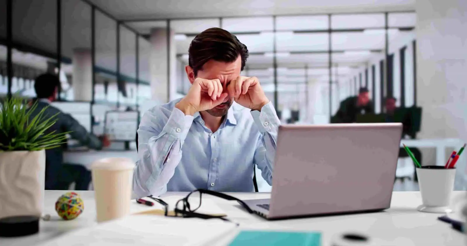 Frustrated businessman at office desk struggling with stress, feeling overwhelmed, expressing disappointment or exhaustion during work in a modern corporate environment.