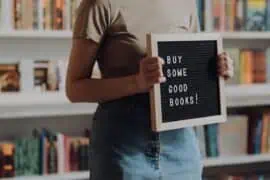 Buy good books sign held by person in a bookstore or library.
