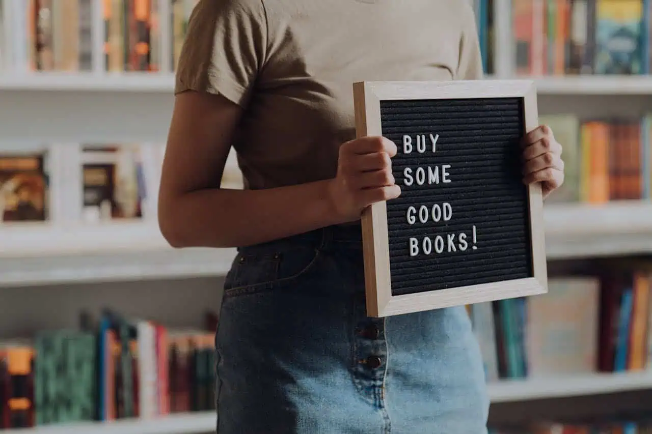 Buy good books sign held by person in a bookstore or library.