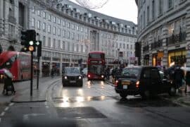 London street scene with buses, cars, and pedestrians on a rainy day, highlighting urban transportation and city environment in the UK.