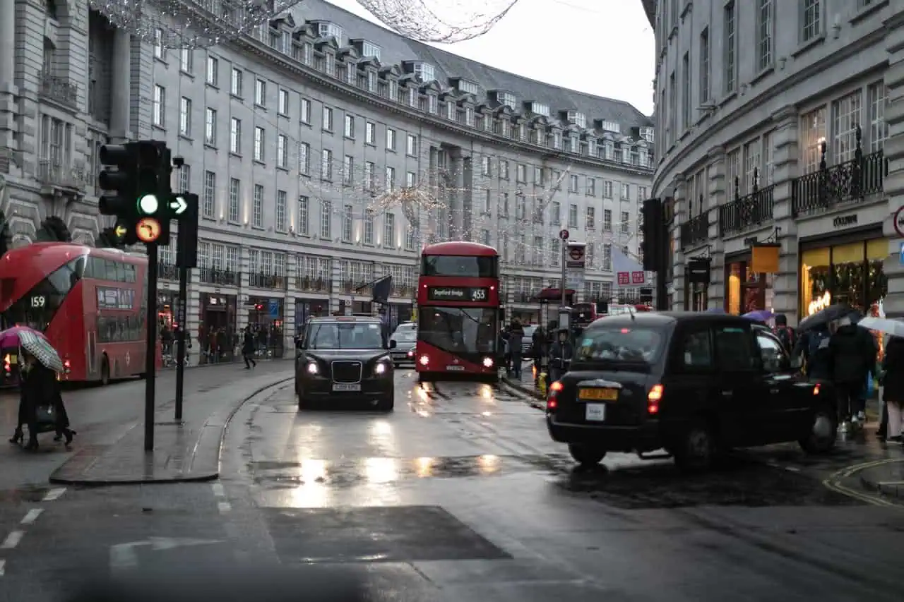 London street scene with buses, cars, and pedestrians on a rainy day, highlighting urban transportation and city environment in the UK.