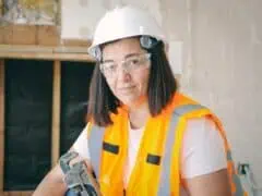 Empowered woman in construction gear working with a power drill on a building site, promoting women in manual trades and encouraging gender diversity in skilled professions.
