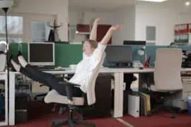Young woman stretching and relaxing at her office desk, highlighting the importance of taking breaks to prevent employee health issues.