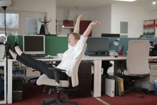 Young woman stretching and relaxing at her office desk, highlighting the importance of taking breaks to prevent employee health issues.
