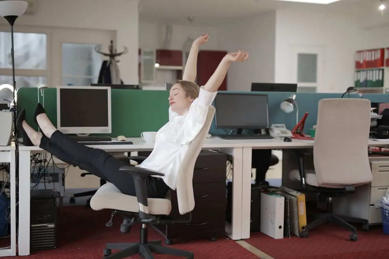 Young woman stretching and relaxing at her office desk, highlighting the importance of taking breaks to prevent employee health issues.