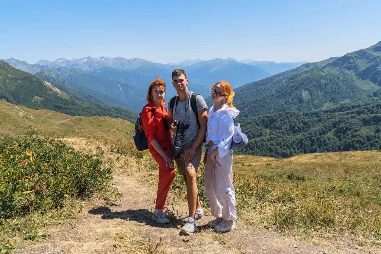 Group of three friends hiking in scenic mountain terrain with lush green hills and distant snow-capped peaks, enjoying outdoor adventure and nature in 2026.