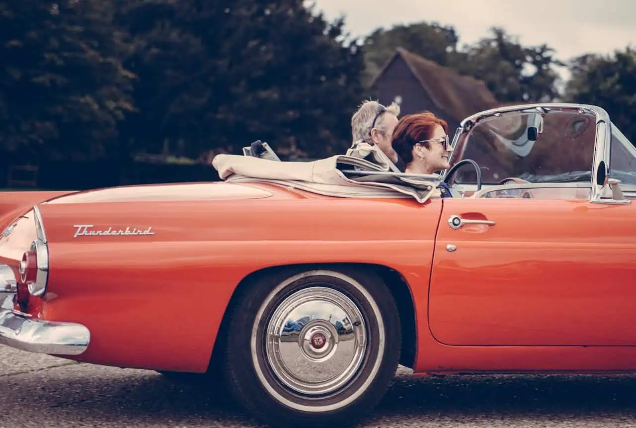A vintage red convertible car with two passengers enjoying a drive, highlighting classic car insurance considerations and common mistakes to avoid for better coverage.