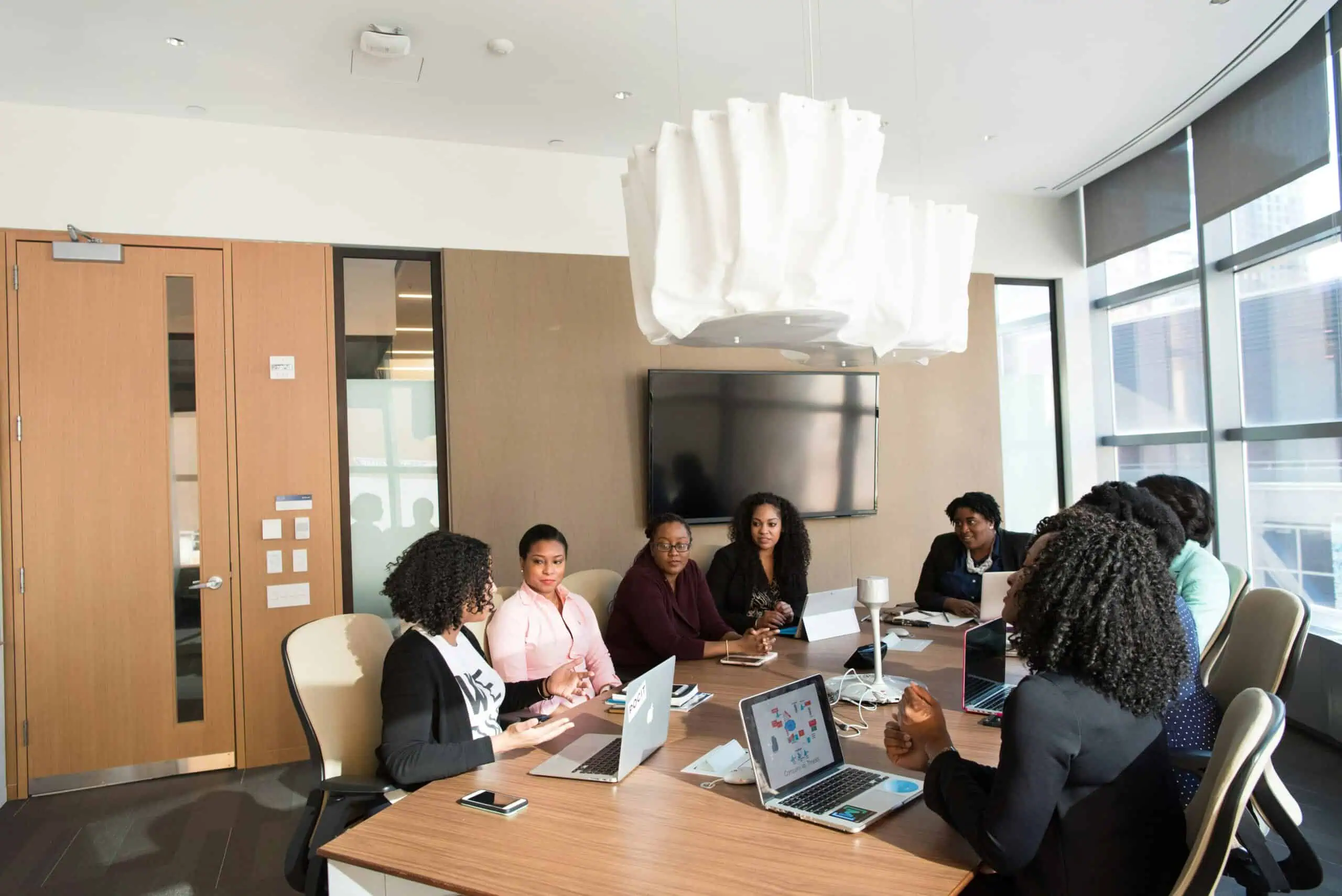 A diverse group of professionals in a business meeting around a conference table with laptops and documents in a modern office setting.