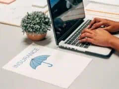 Close-up of a person typing on a laptop with insurance documents and a potted plant on a desk, representing professional insurance planning services.