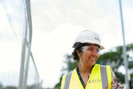 A tradeswoman going through the construction site in a helmet and smiling