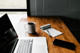 Office table with laptop, coffee mug, smartphone, small notebook and a pen