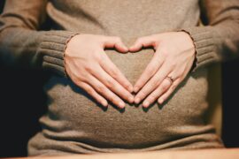 A pregnant woman holding hangs in a heart shape over the belly