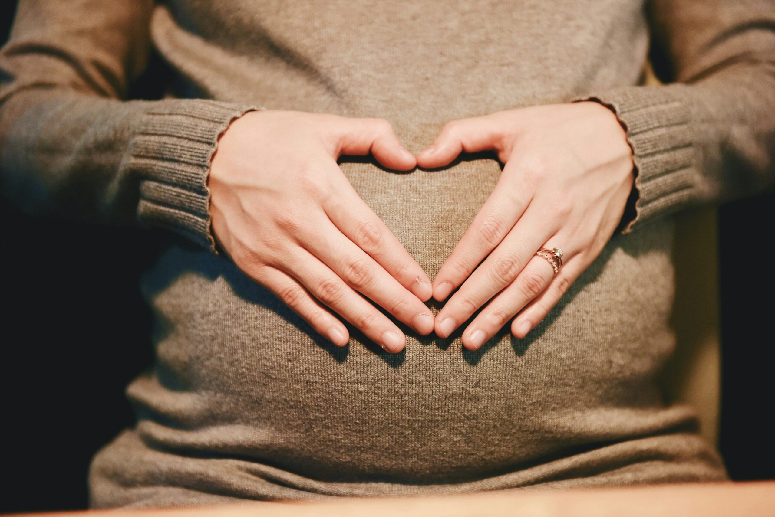 A pregnant woman holding hangs in a heart shape over the belly