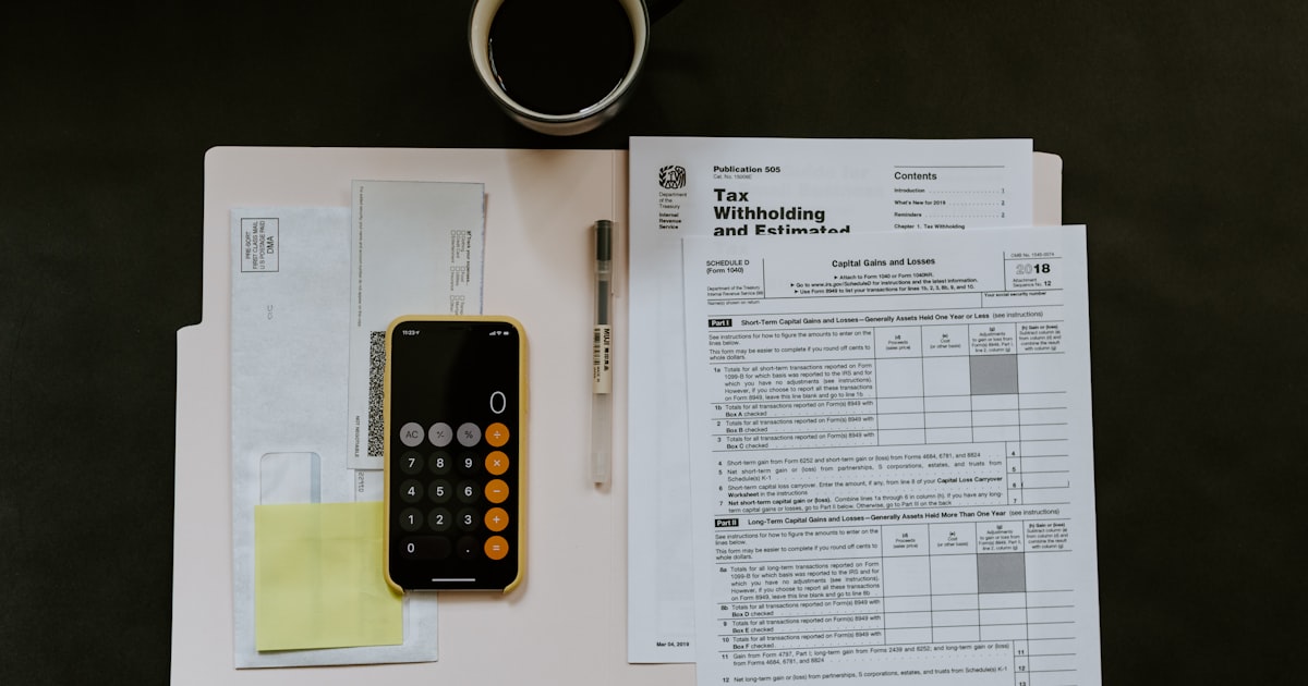 black Android smartphone near ballpoint pen, tax withholding certificate on top of white folder