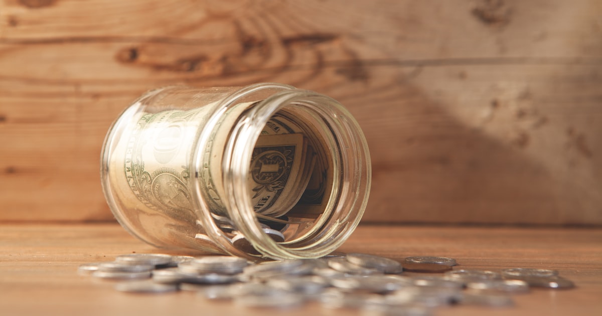 Glass jar with money and coins spilled on table