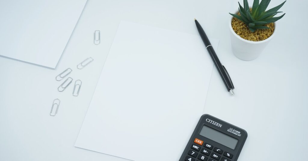 A financial and money themed photo featuring a blank paper on a desk next to a pen and calculator. Crunch the numbers!