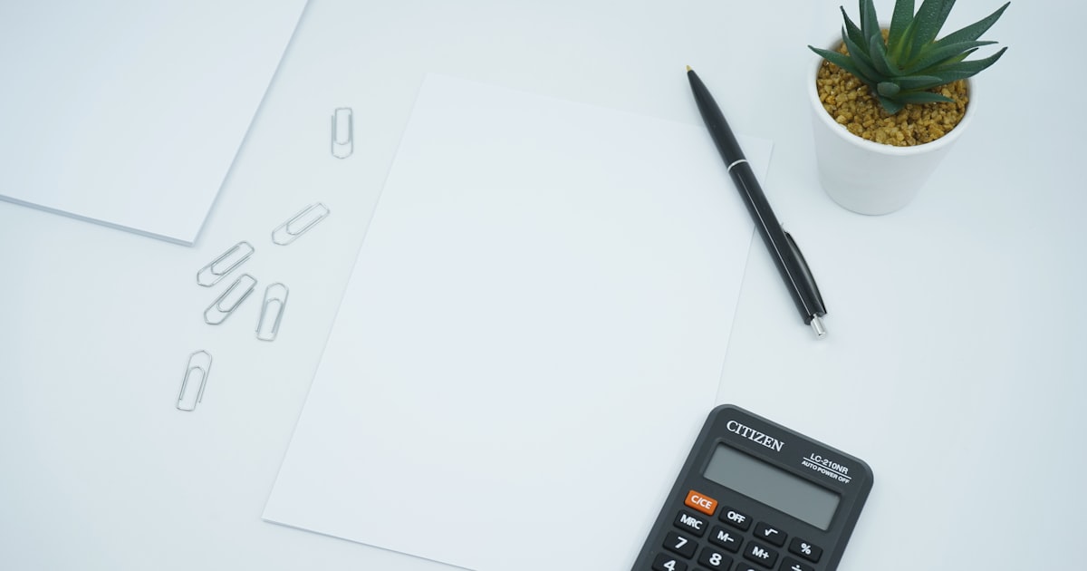 A financial and money themed photo featuring a blank paper on a desk next to a pen and calculator. Crunch the numbers!