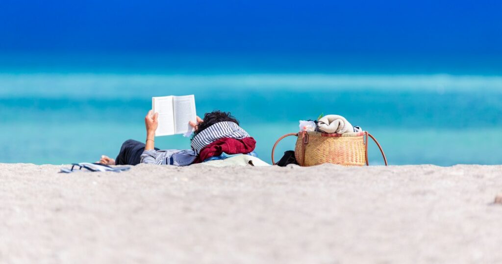 A calm scene featuring a person reading a book on the beach.