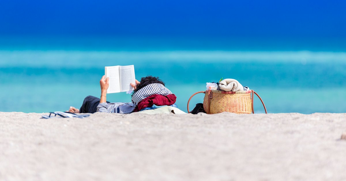 A calm scene featuring a person reading a book on the beach.