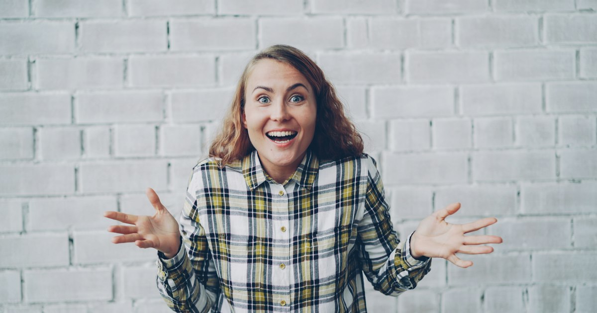 Portrait of happy and excited young woman smiling, laughing, opening mouth and touching face expressing excitement and happiness. Good news and positive emotions concept.